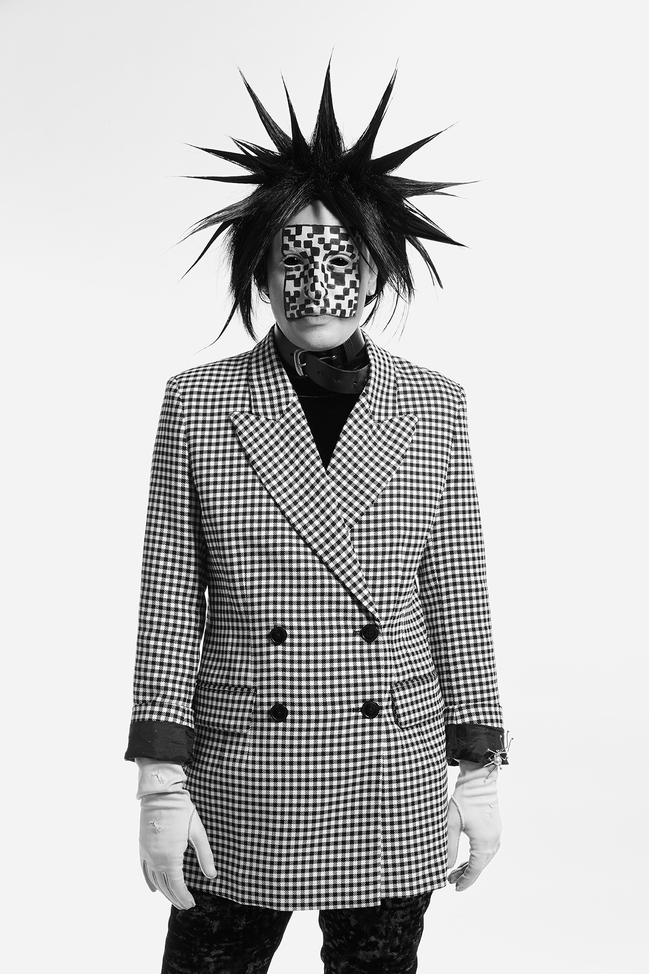 Jesse facing the camera with checkered facepaint, spiked black hair and a checkered blazer on a white background
